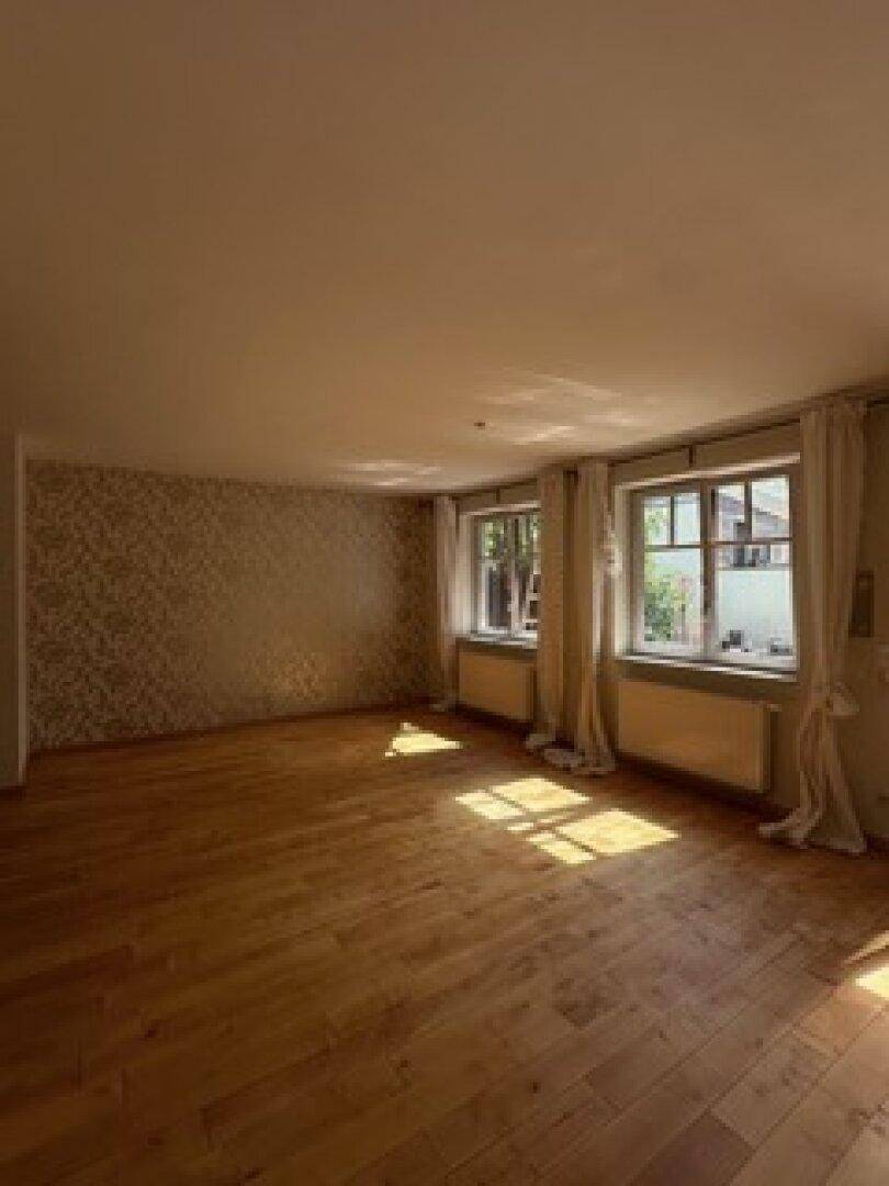 Heller Wohnraum mit Holzboden, gemusterter Tapete und großen Fenstern für viel Tageslicht.