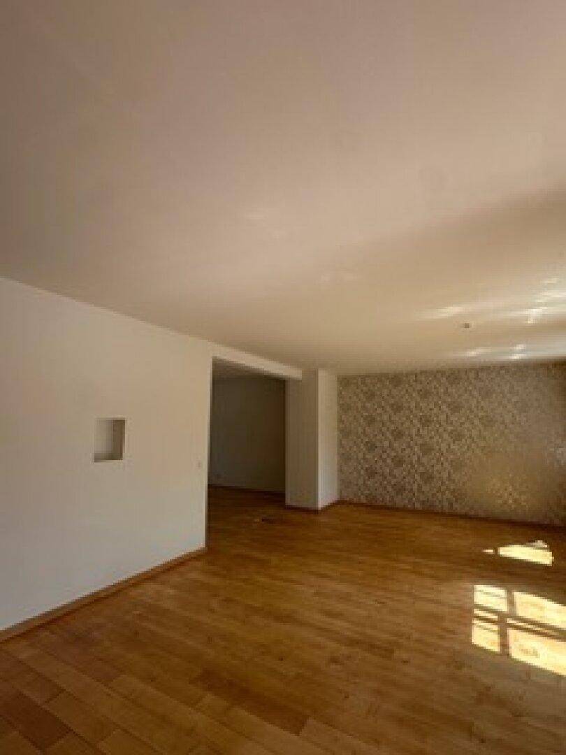 Geräumiger, leerer Raum mit hellem Holzfußboden und einer Wand mit dezenter Tapete.