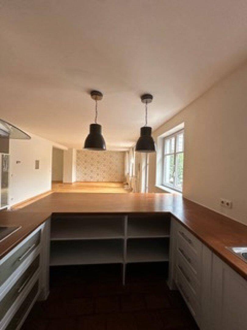 Offene Küche mit weißen Unterschränken, Holz-Arbeitsplatten und Blick in den Wohnbereich.