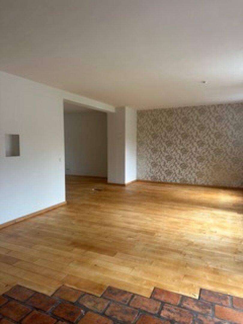 Geräumiges Wohnzimmer mit Holzboden und einer Wand mit dekorativer Tapete, bereit zur individuellen Gestaltung.