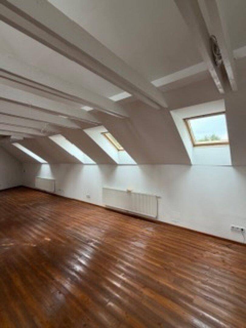 Dachgeschossraum mit sichtbaren Holzbalken, schrägen Wänden und mehreren Dachfenstern für viel Helligkeit.