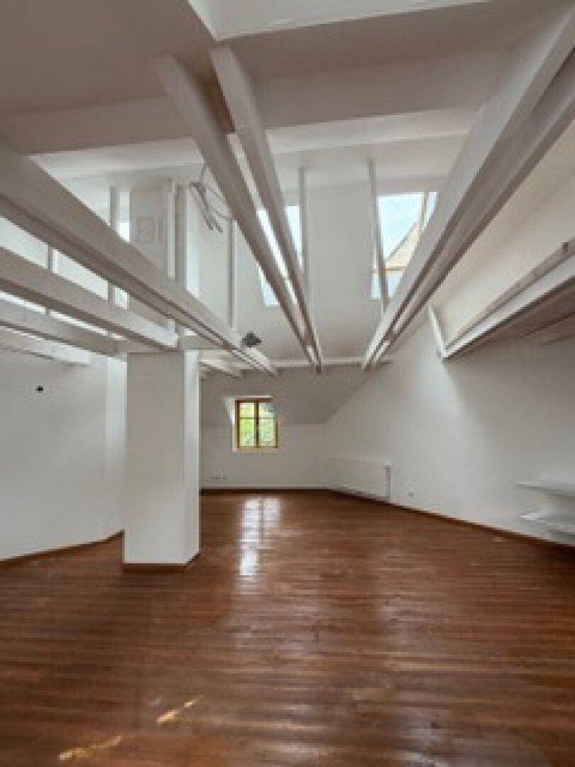 Geräumiges Dachgeschoss mit hohen Decken, sichtbaren Holzbalken und einem Fenster, das den Raum erhellt.