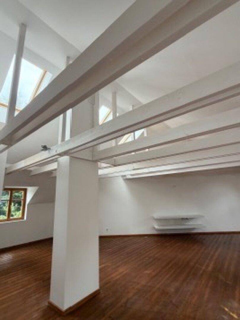 Heller Dachgeschossraum mit sichtbaren Holzbalken, Dachfenstern und integrierten Regalen für zusätzlichen Stauraum.