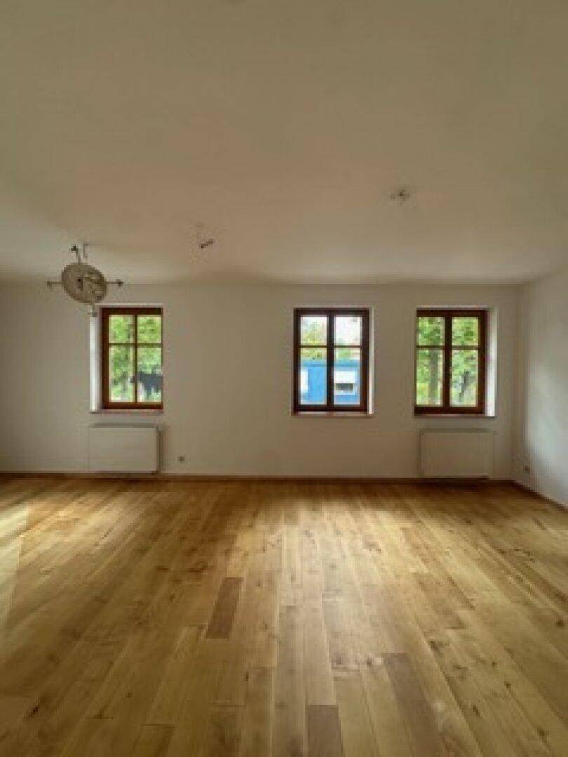 Heller Raum mit Holzboden und drei Fenstern, die eine angenehme Atmosphäre schaffen und viel Licht spenden.