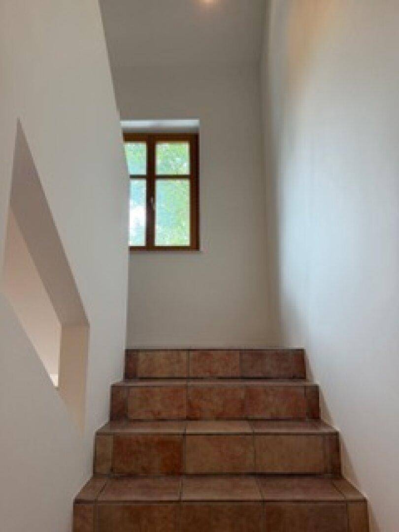 Treppenhaus mit braunen Fliesenstufen und einem Fenster, das den Bereich mit natürlichem Licht versorgt.