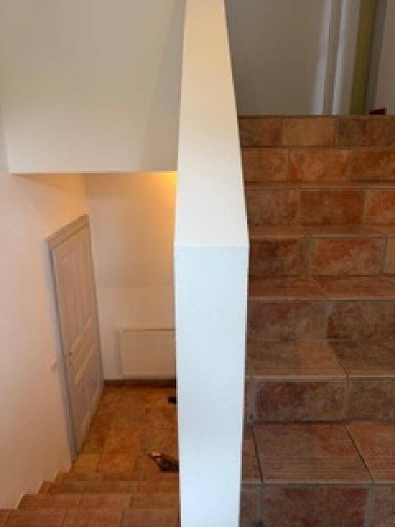 Treppenbereich mit gefliesten Stufen und einer Tür unter der Treppe, die zu einem weiteren Raum führt.
