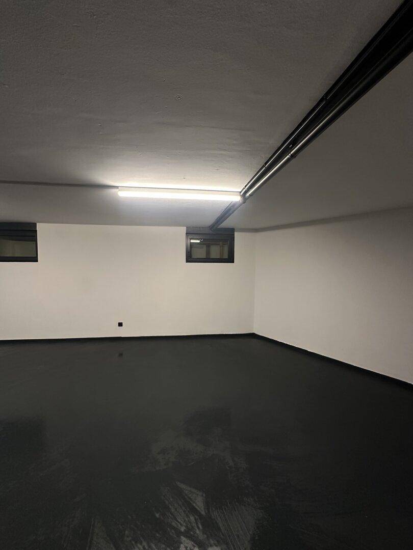 Geräumiger Kellerraum mit dunklem Boden, weißen Wänden und funktionaler Beleuchtung, ideal als Lagerfläche.