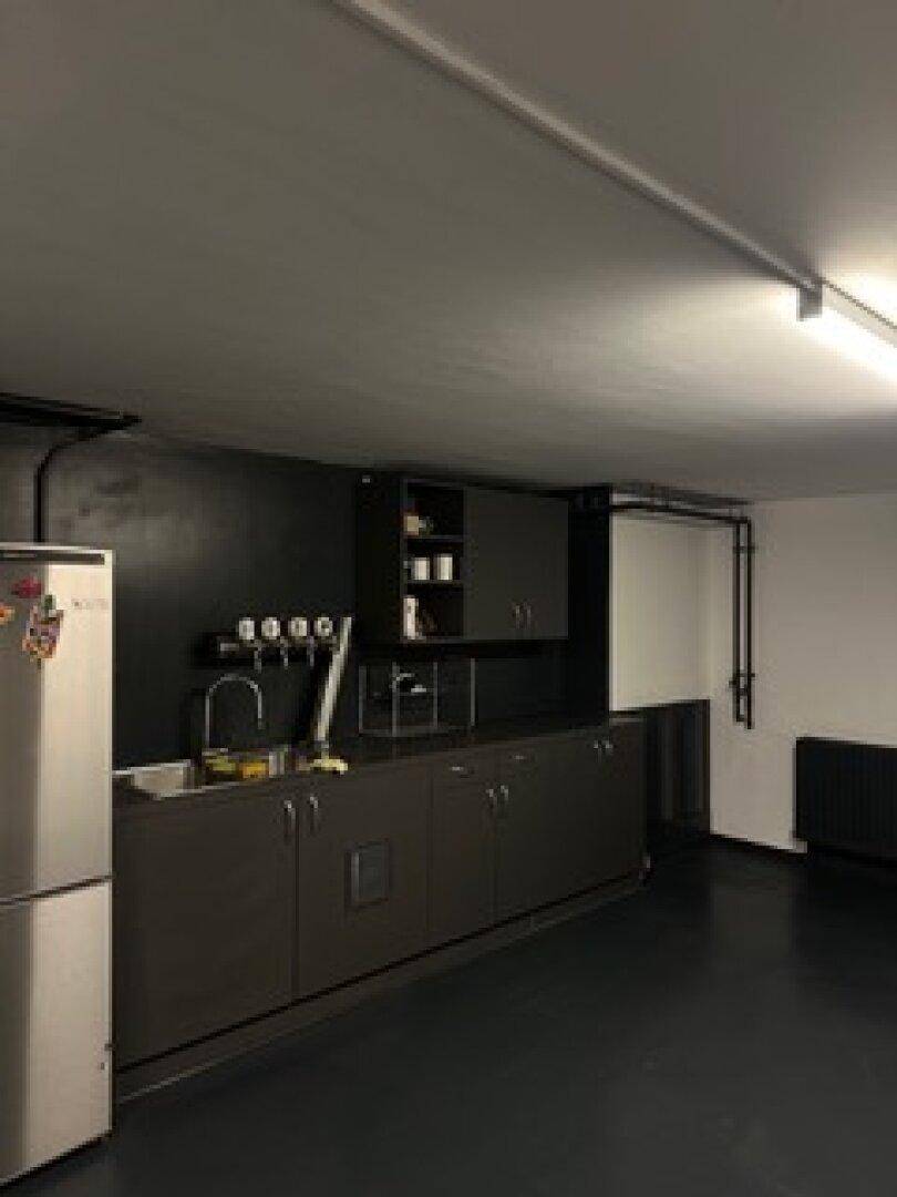 Kellerraum mit dunklen Schränken, Spüle und Kühlschrank, der als zusätzliche Küchenzeile oder Bar genutzt werden kann.