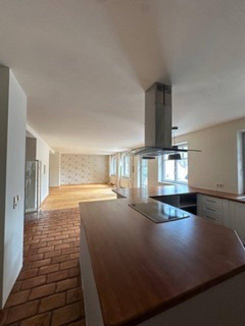 Offener Wohn- und Essbereich mit Kücheninsel, Terrakotta-Fliesenboden und Holzboden im Hintergrund.