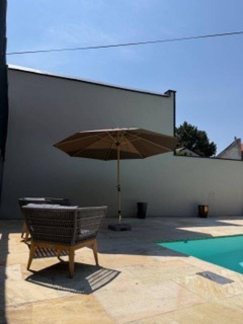 Detailansicht des Poolbereichs mit modernen Outdoor-Möbeln und großem Sonnenschirm.
