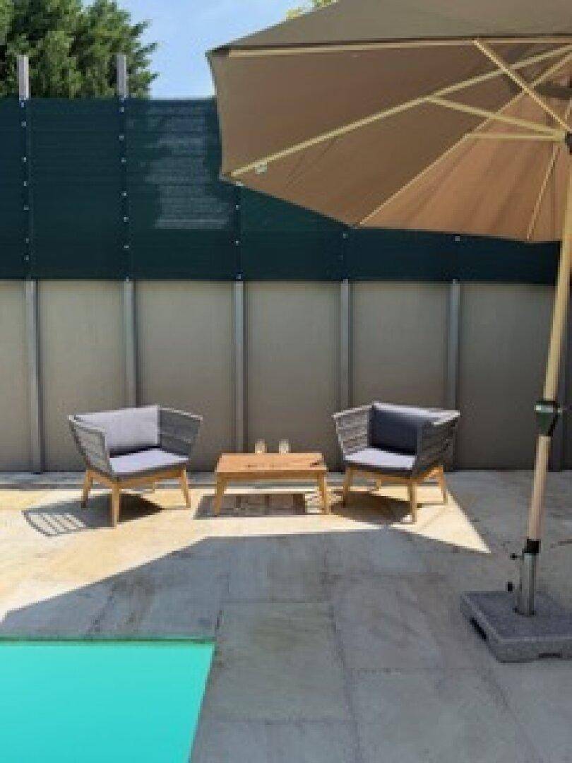 Sonniger Terrassenbereich mit bequemen Outdoor-Sitzmöbeln, großem Sonnenschirm und Blick auf den Pool.