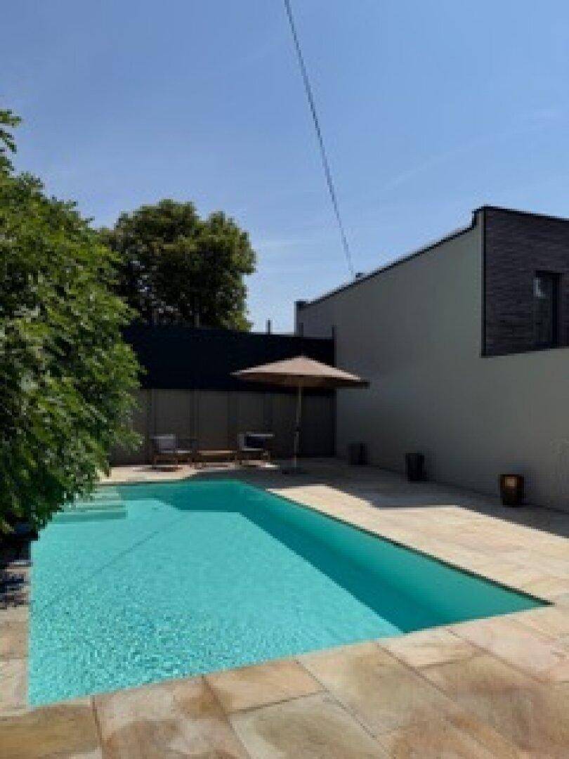 Großer Außenpool mit gepflasterter Terrasse und moderner Gebäudearchitektur an einem sonnigen Tag.