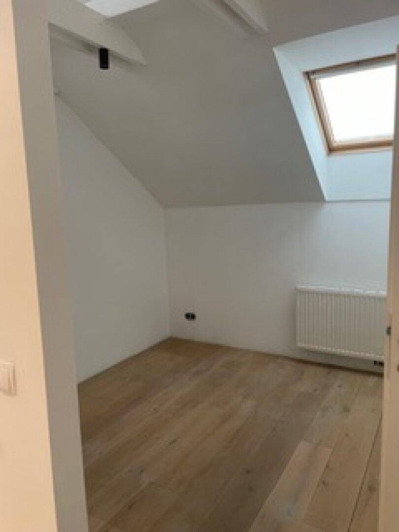 Kleines Schlafzimmer im Dachgeschoss mit Holzboden, schräger Decke und einem Dachfenster, das den Raum erhellt.
