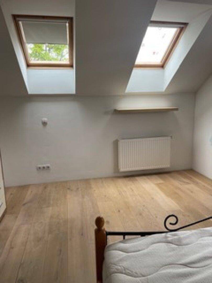 Helles Schlafzimmer im Dachgeschoss mit Holzboden, schrägen Wänden und zwei Dachfenstern für viel Licht.