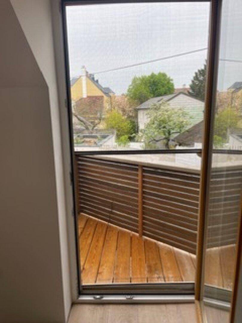 Kleiner Balkon mit Holzboden und Blick auf die umliegende Nachbarschaft mit Bäumen und Häusern.