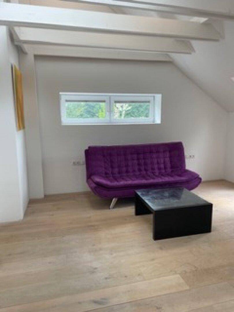 Gemütlicher Wohnbereich im Dachgeschoss mit Holzboden, sichtbaren Balken und einem farbenfrohen Sofa.