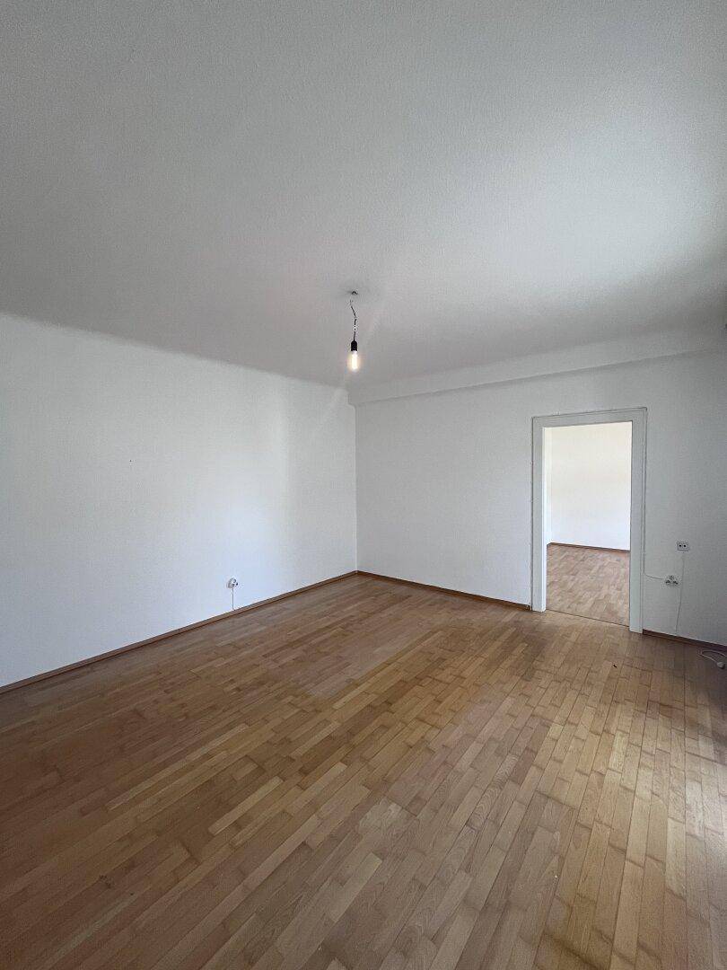 Heller, leerer Raum mit Parkettboden, der sich ideal als Wohnzimmer eignet.