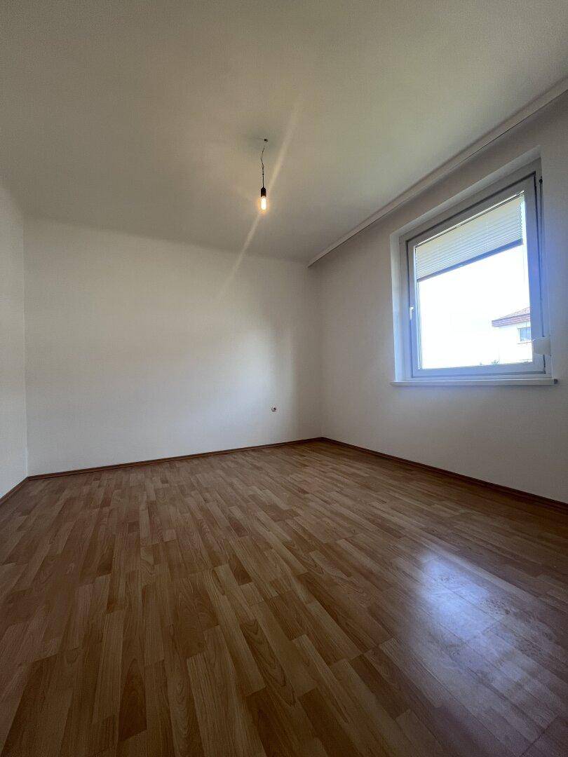 Helles Schlafzimmer mit Parkettboden und einem Fenster, das viel Tageslicht hereinlässt.