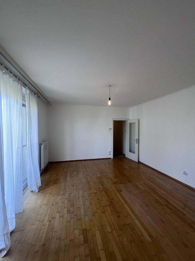 Großzügiger, heller Raum mit Parkettboden und viel Tageslicht, ideal als Wohnbereich.