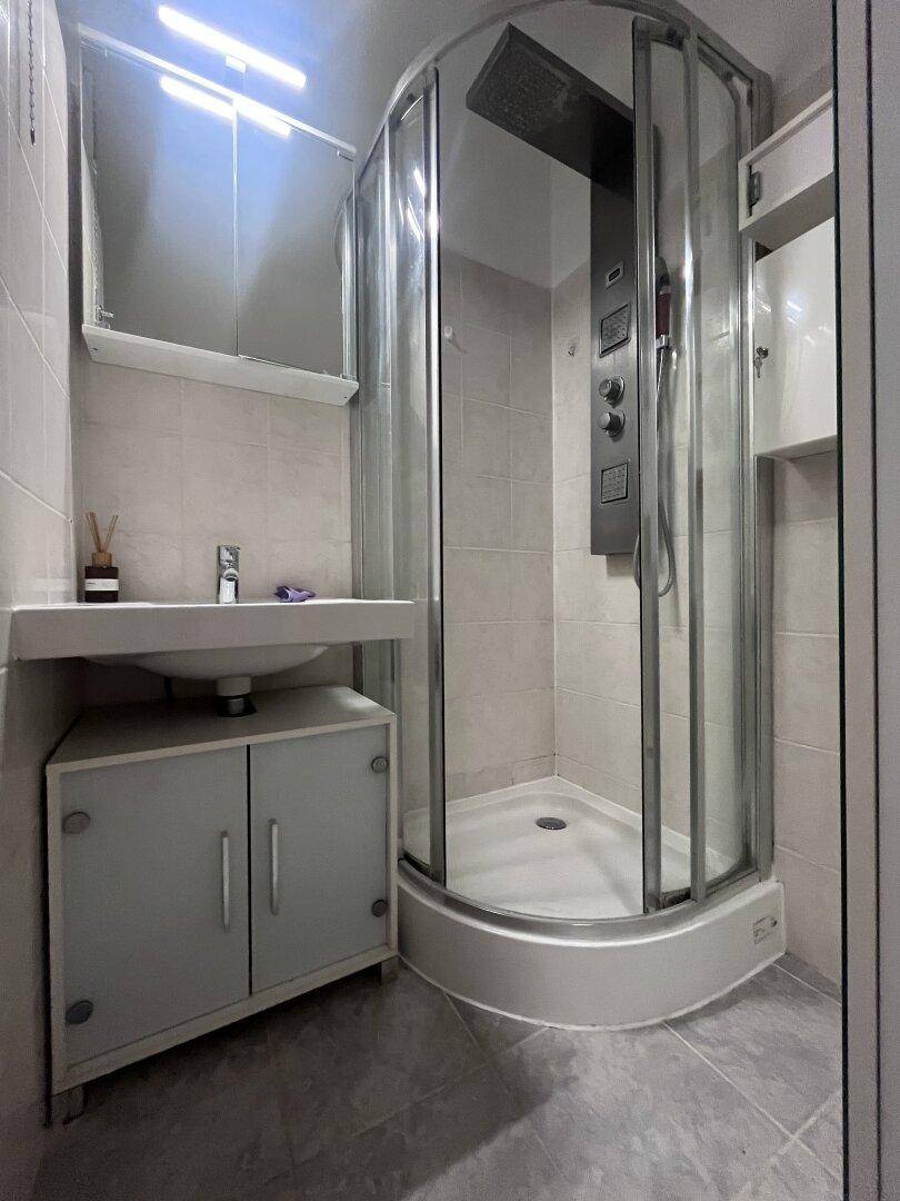 Funktionales Badezimmer mit Eckduschkabine, Waschbecken und praktischem Stauraum.