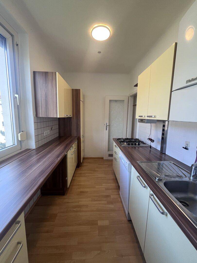Funktionale Küche mit Gasherd, Spüle und hellen Schränken, gut beleuchtet durch ein Fenster.