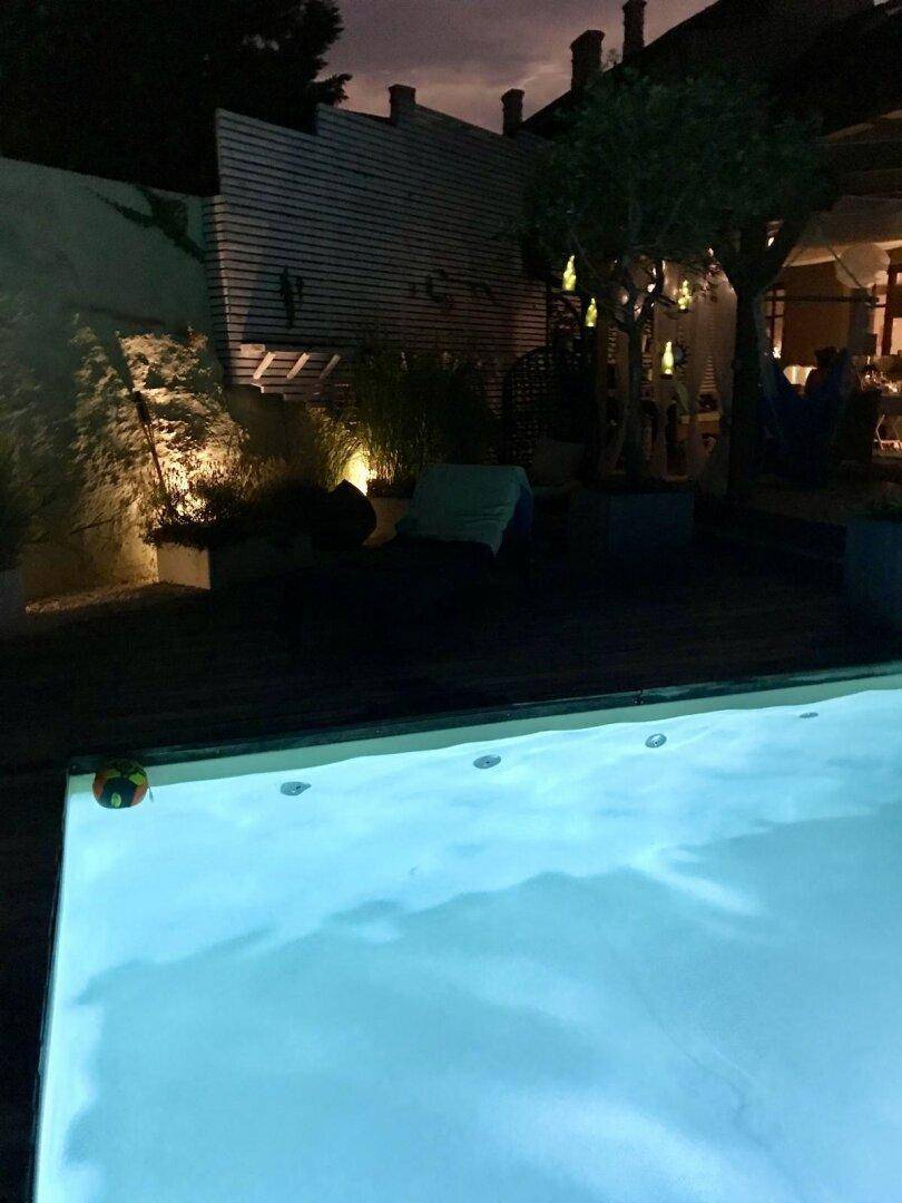 Weitläufiger Pool- und Gartenbereich bei Nacht mit stimmungsvoller Beleuchtung und Bäumen.