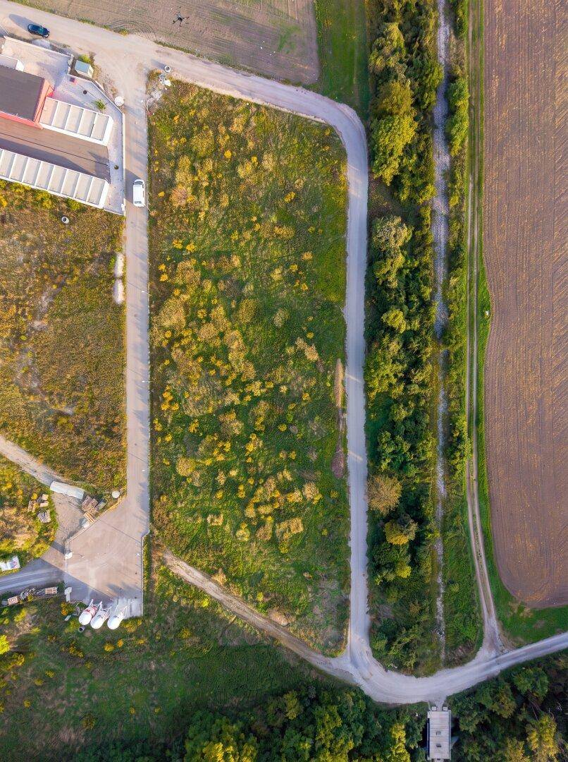 Luftaufnahme eines unbebauten Grundstücks mit angrenzenden Wegen und grüner Vegetation bei Tageslicht.
