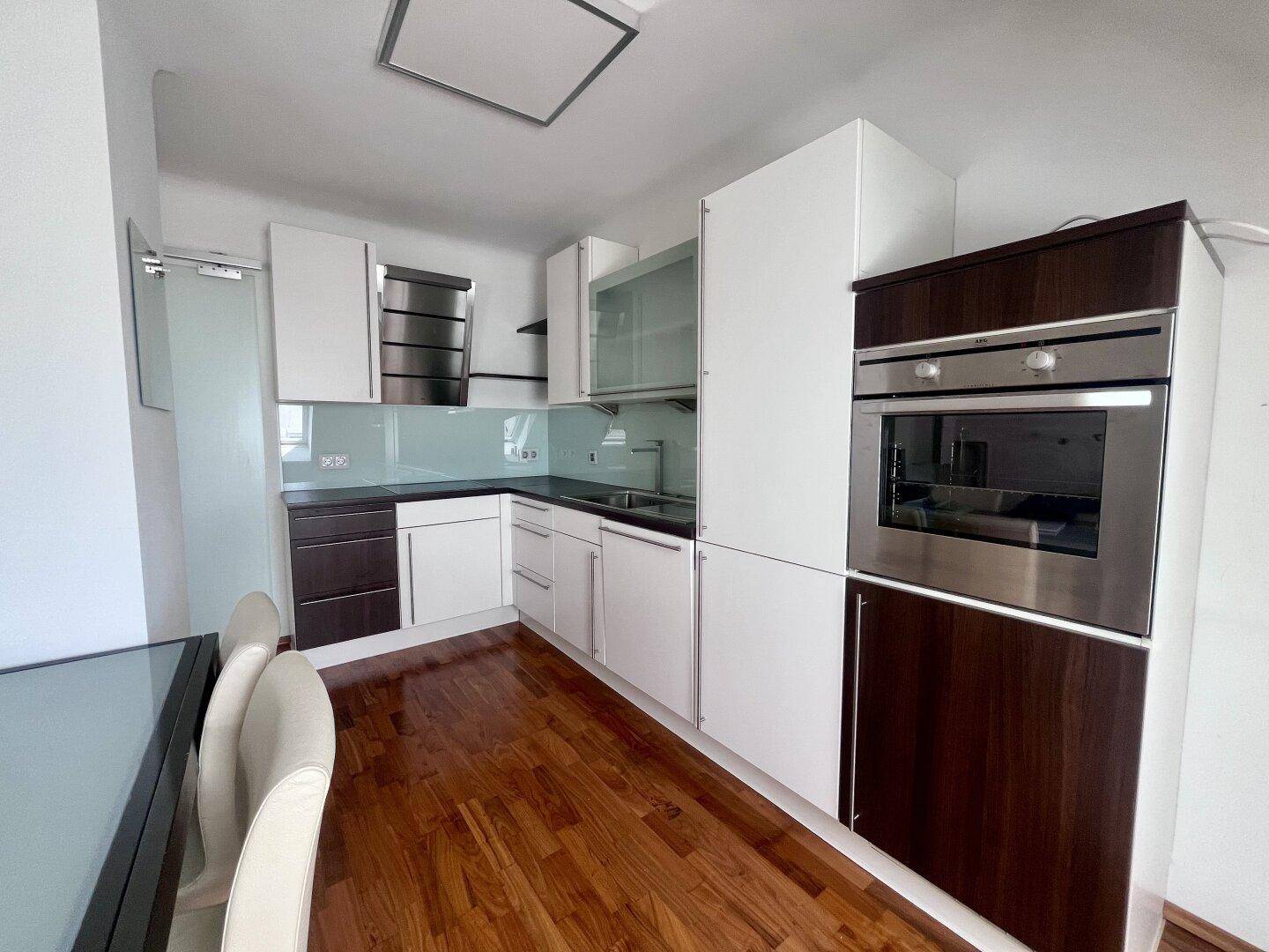 Moderne Küche mit weißen und dunklen Schränken, integriertem Backofen und Holzboden.
