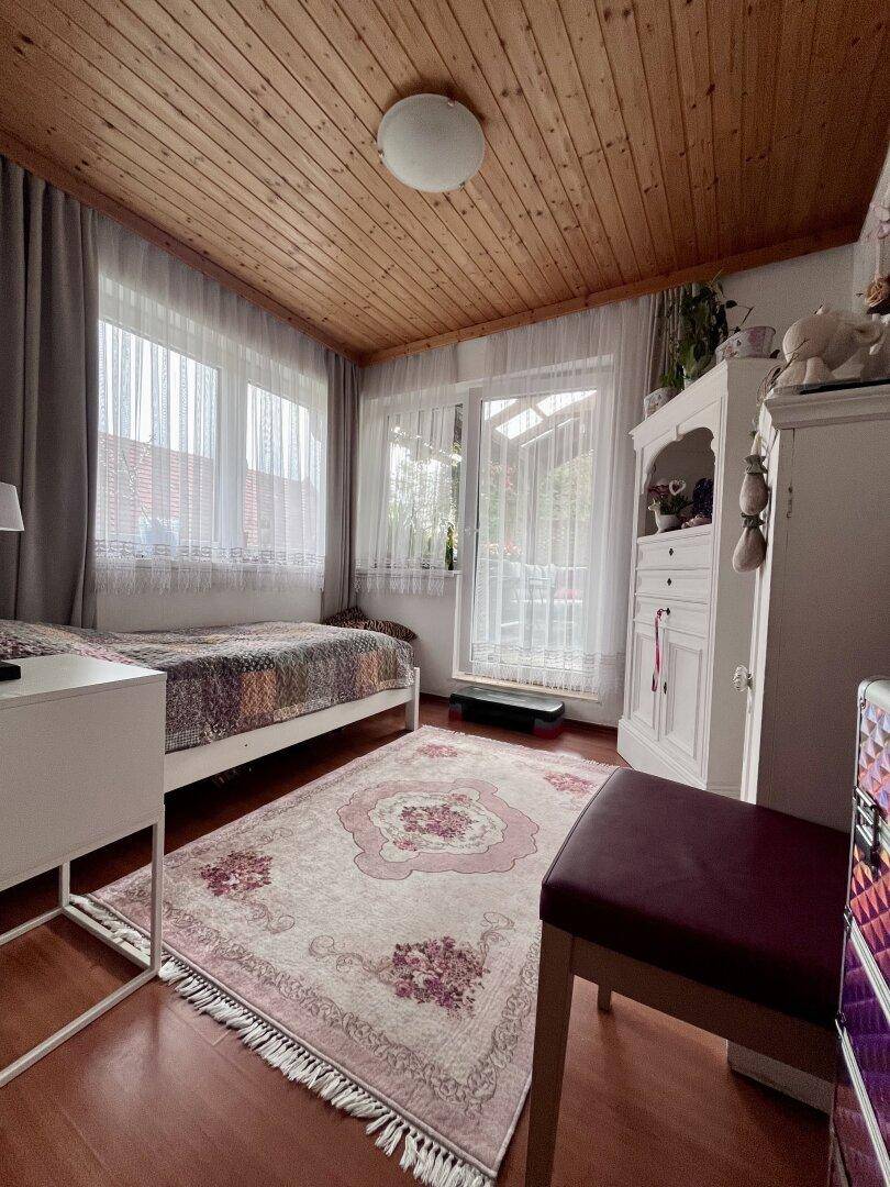 Helles Schlafzimmer mit Einzelbett, Holzdecke und Zugang zum Balkon.