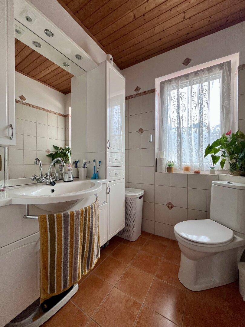 Badezimmer mit Waschtisch, Toilette, Spiegelschrank und Fenster.