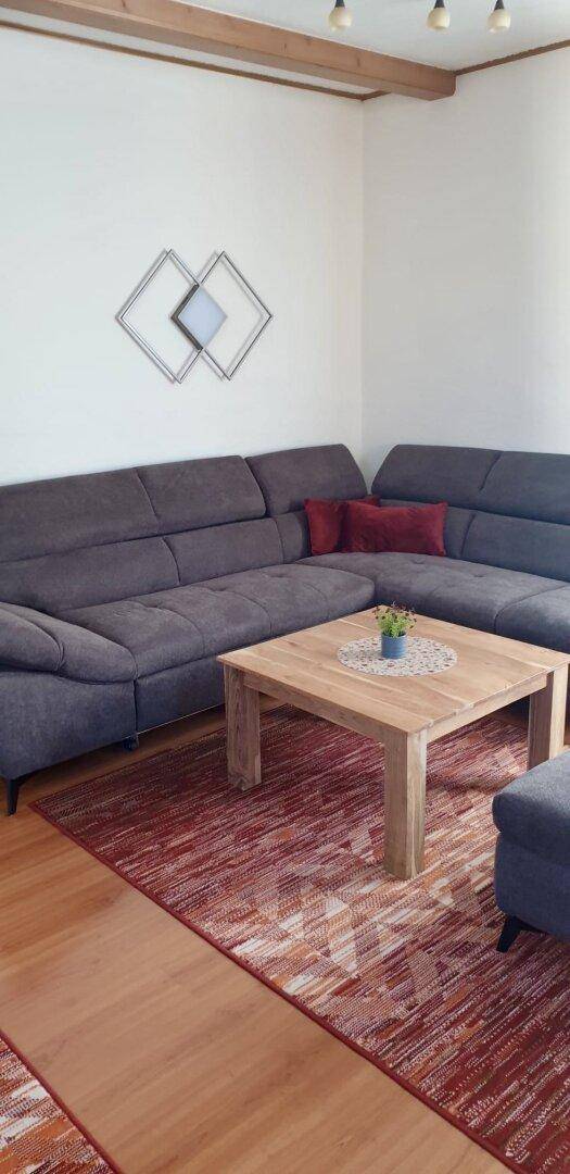 Gemütliches Wohnzimmer mit großem Ecksofa und Holztisch auf Teppichboden.