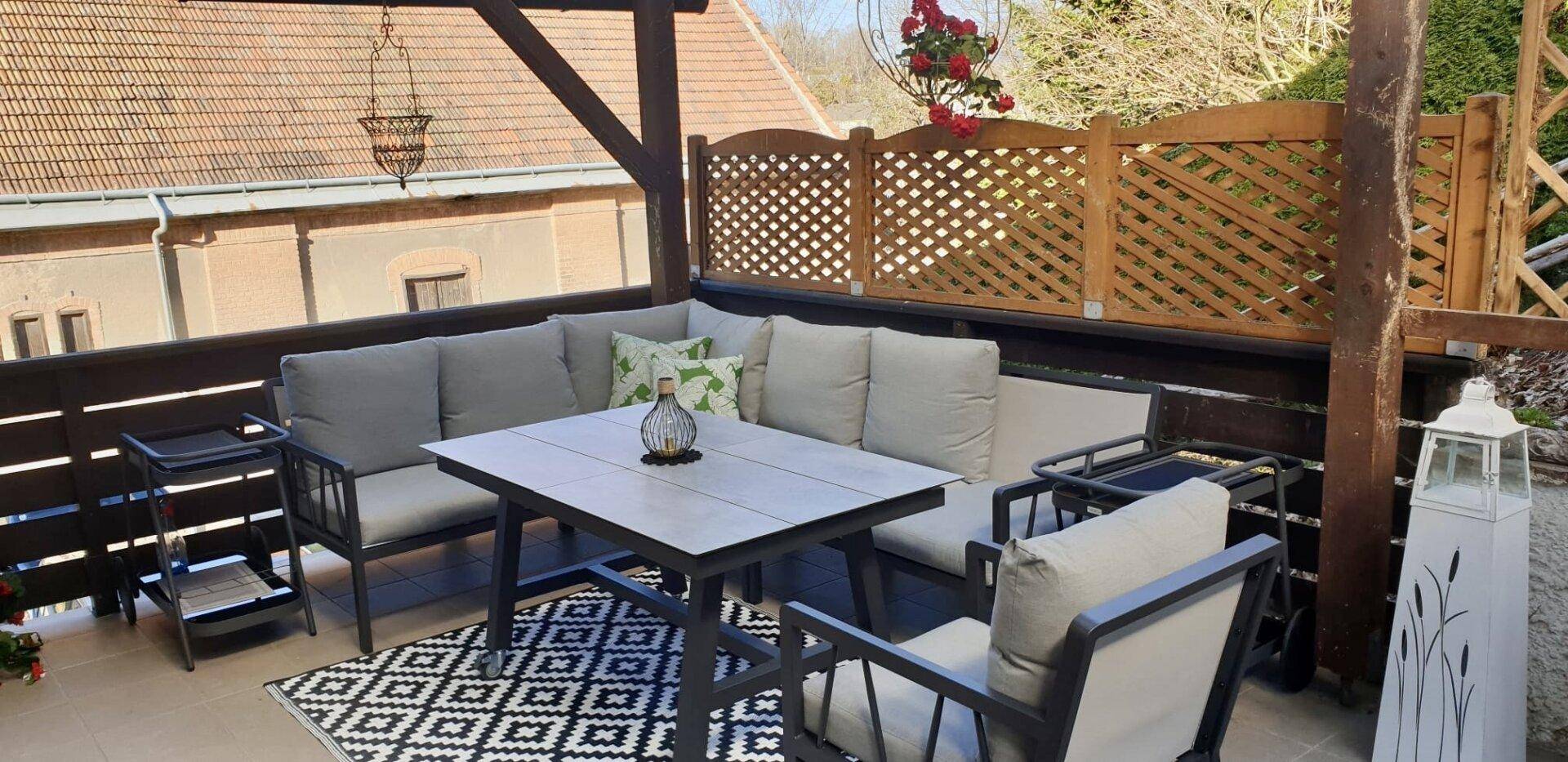 Überdachte Terrasse mit bequemen Gartenmöbeln und Blick auf die Umgebung.