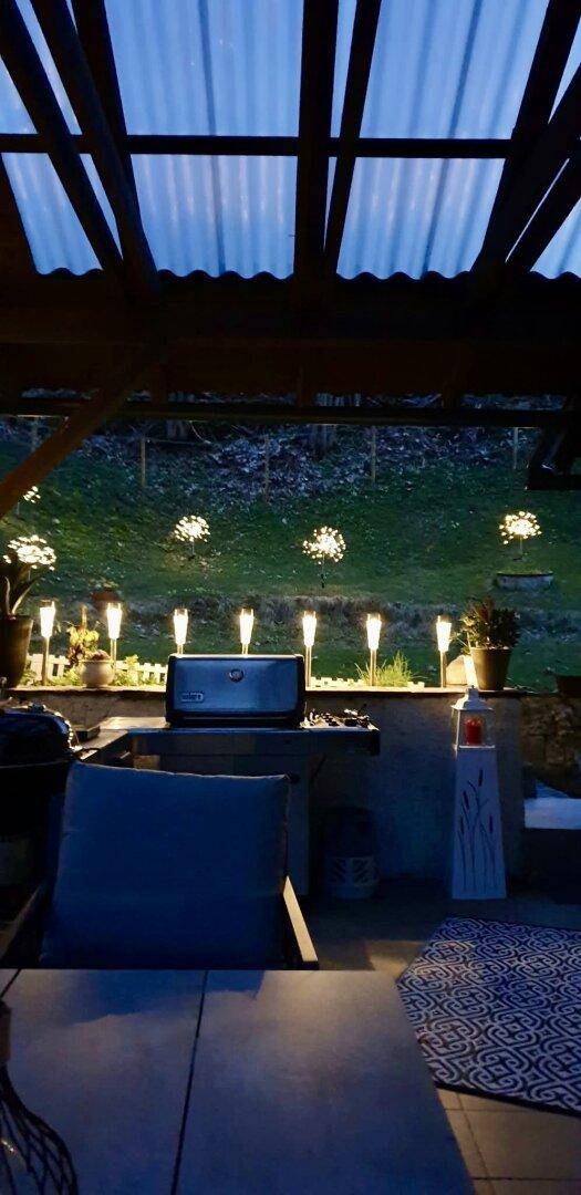 Beleuchtete Terrasse am Abend mit Grillbereich und Blick in den Garten.