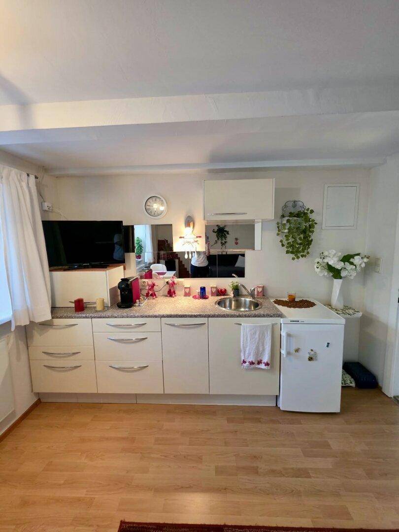 Kleine Küchenzeile mit weißen Schränken, Spüle und Kühlschrank.
