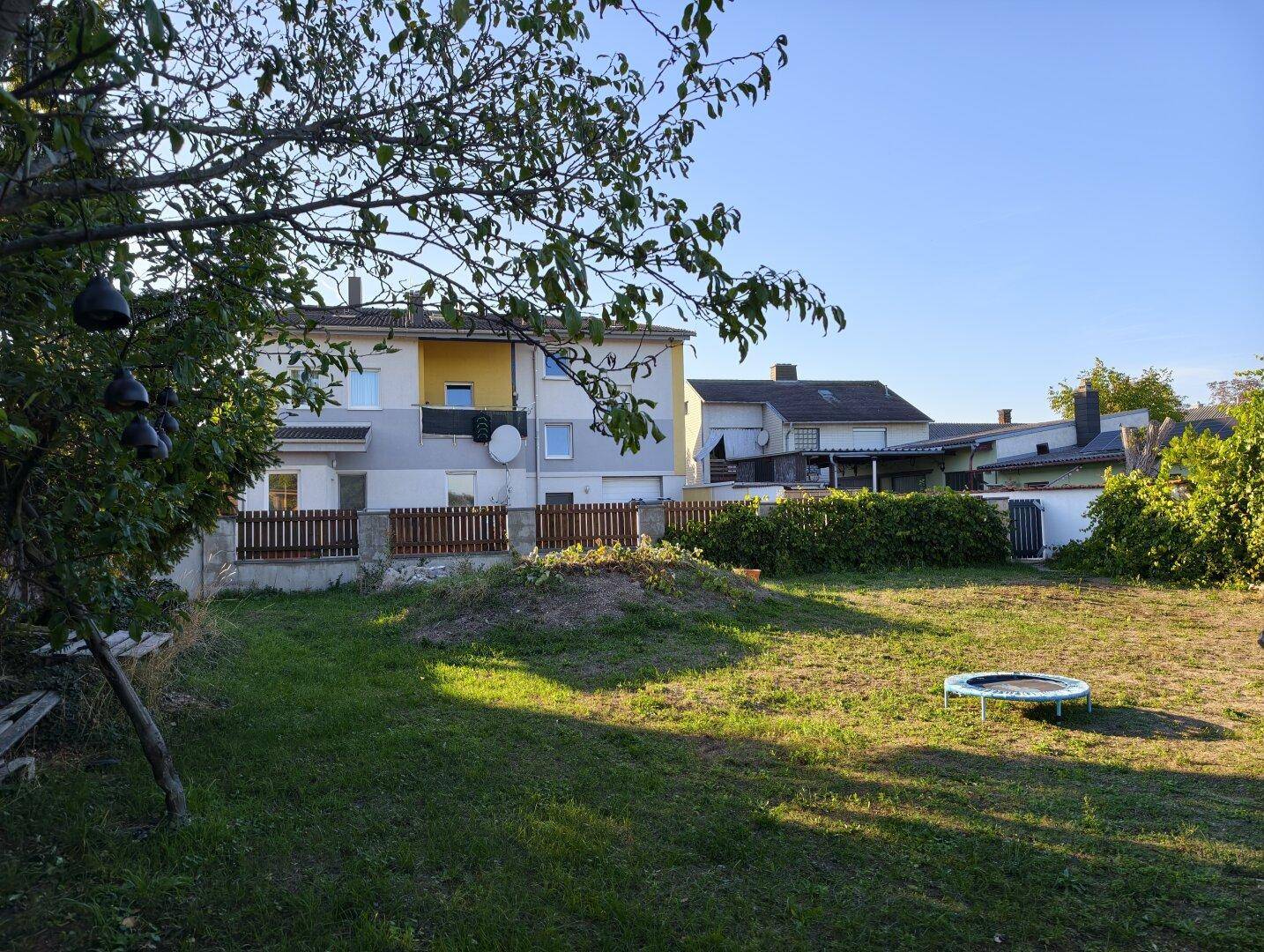 Große Rasenfläche im Garten mit Trampolin und Blick auf das angrenzende Wohnhaus.