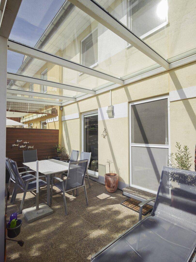 Überdachte Terrasse mit Glasdach, Gartenmöbeln und Zugang zum Haus.