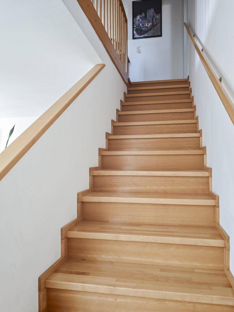 Helle Holztreppe mit Geländer, die in die obere Etage führt und ein Bild an der Wand zeigt.