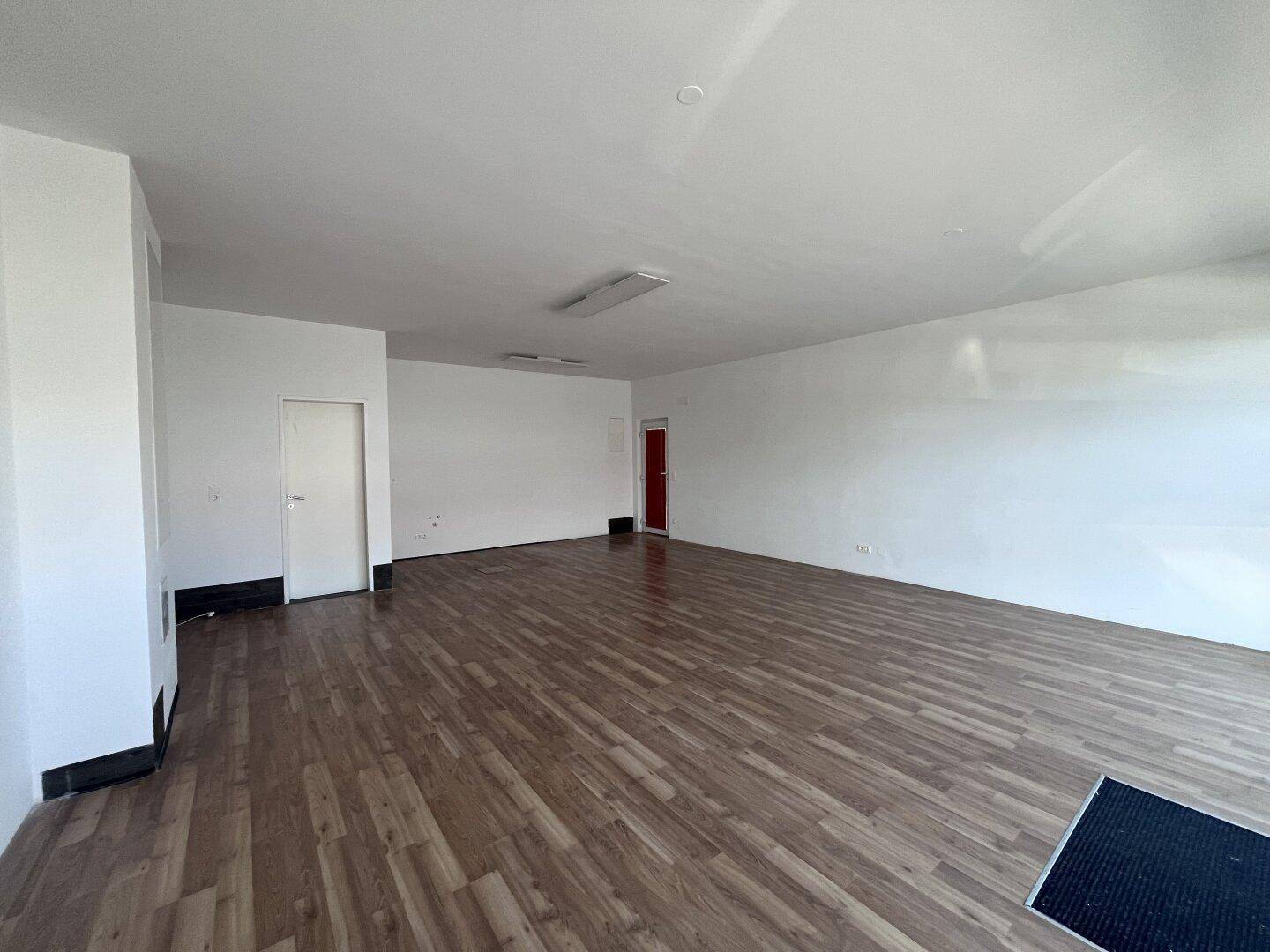 Großer, leerer Gewerberaum mit hellem Laminatboden und weißen Wänden, bereit zur individuellen Gestaltung.