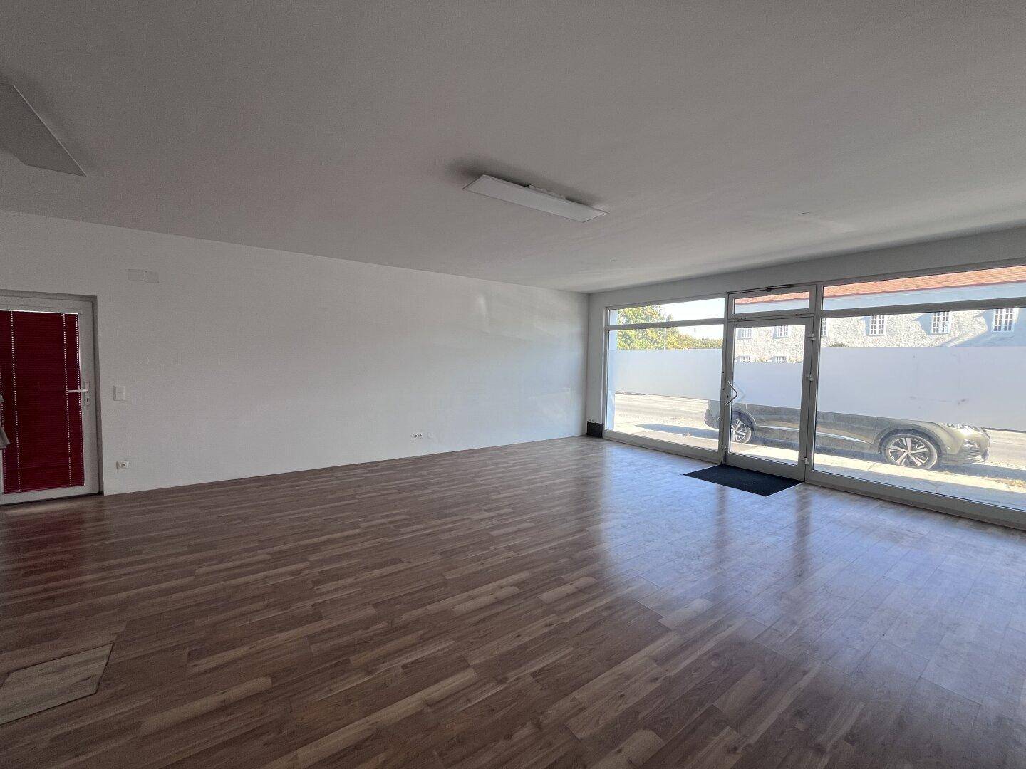 Heller Gewerberaum mit großen Schaufenstern zur Straße und modernem Laminatboden.