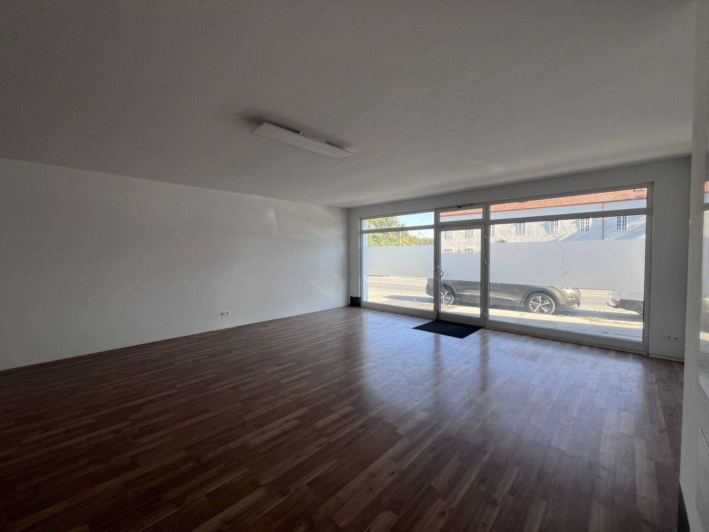 Geräumiger Gewerberaum mit viel Tageslicht durch die großen Fensterfronten und Holzbodenoptik.