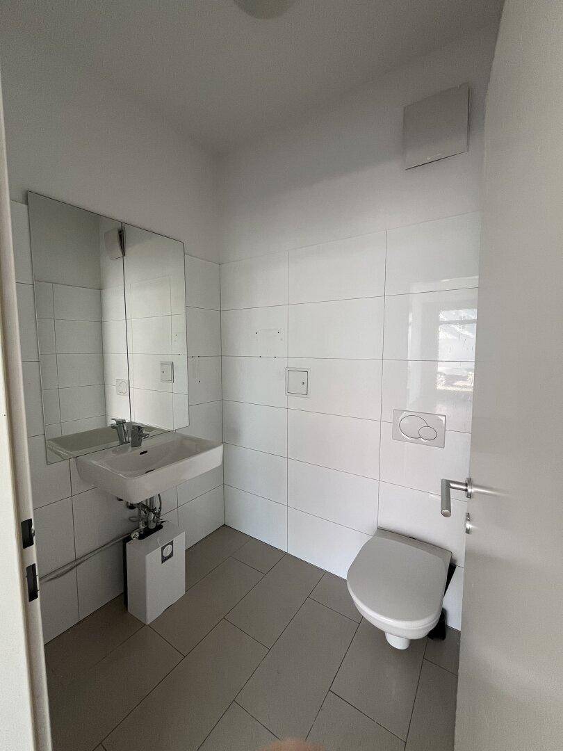 Modernes Gäste-WC mit weißen Fliesen, wandhängendem WC und Waschbecken mit Spiegel.