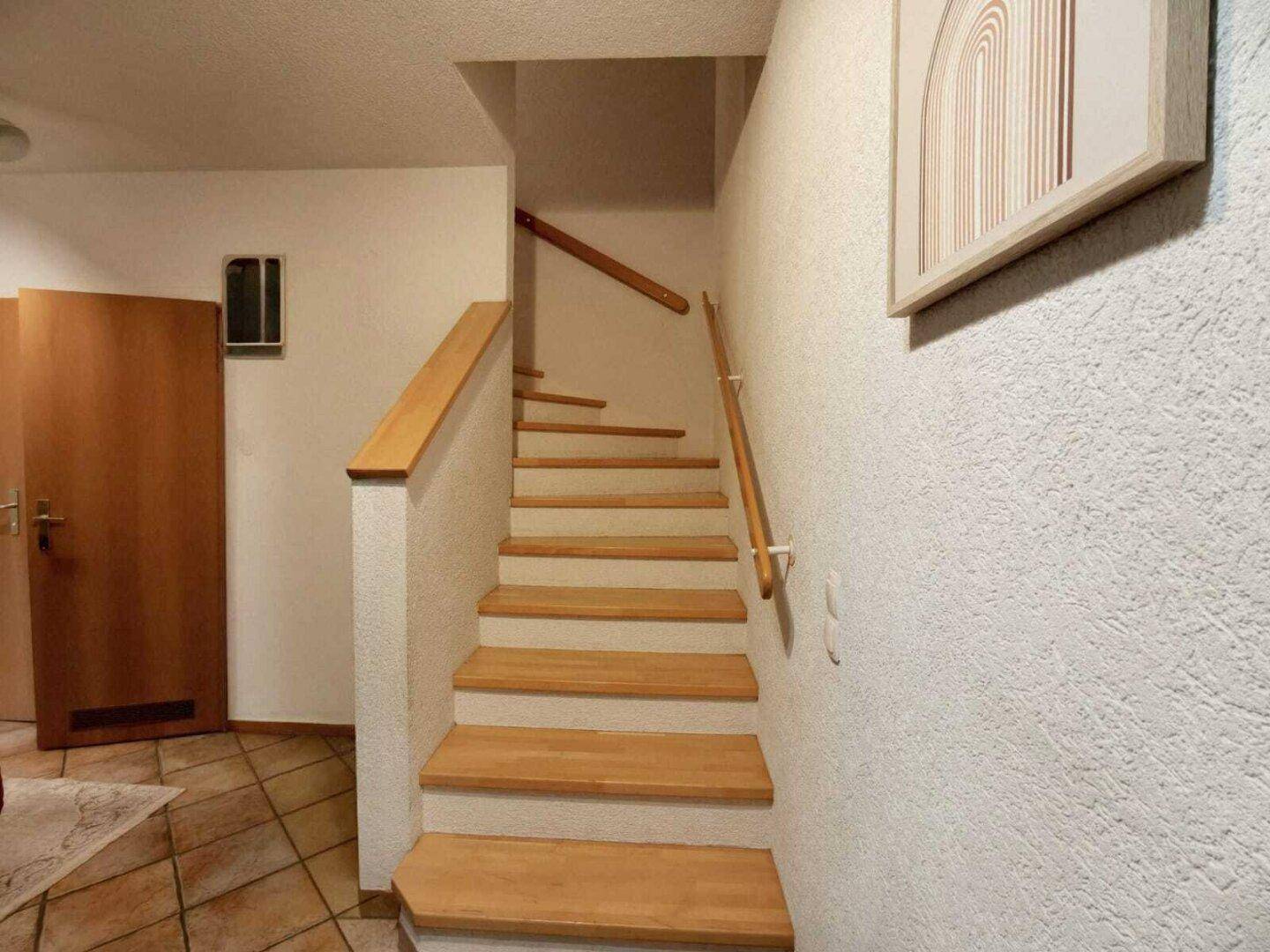 Holztreppe mit hellem Geländer, die in die obere Etage des Hauses führt.