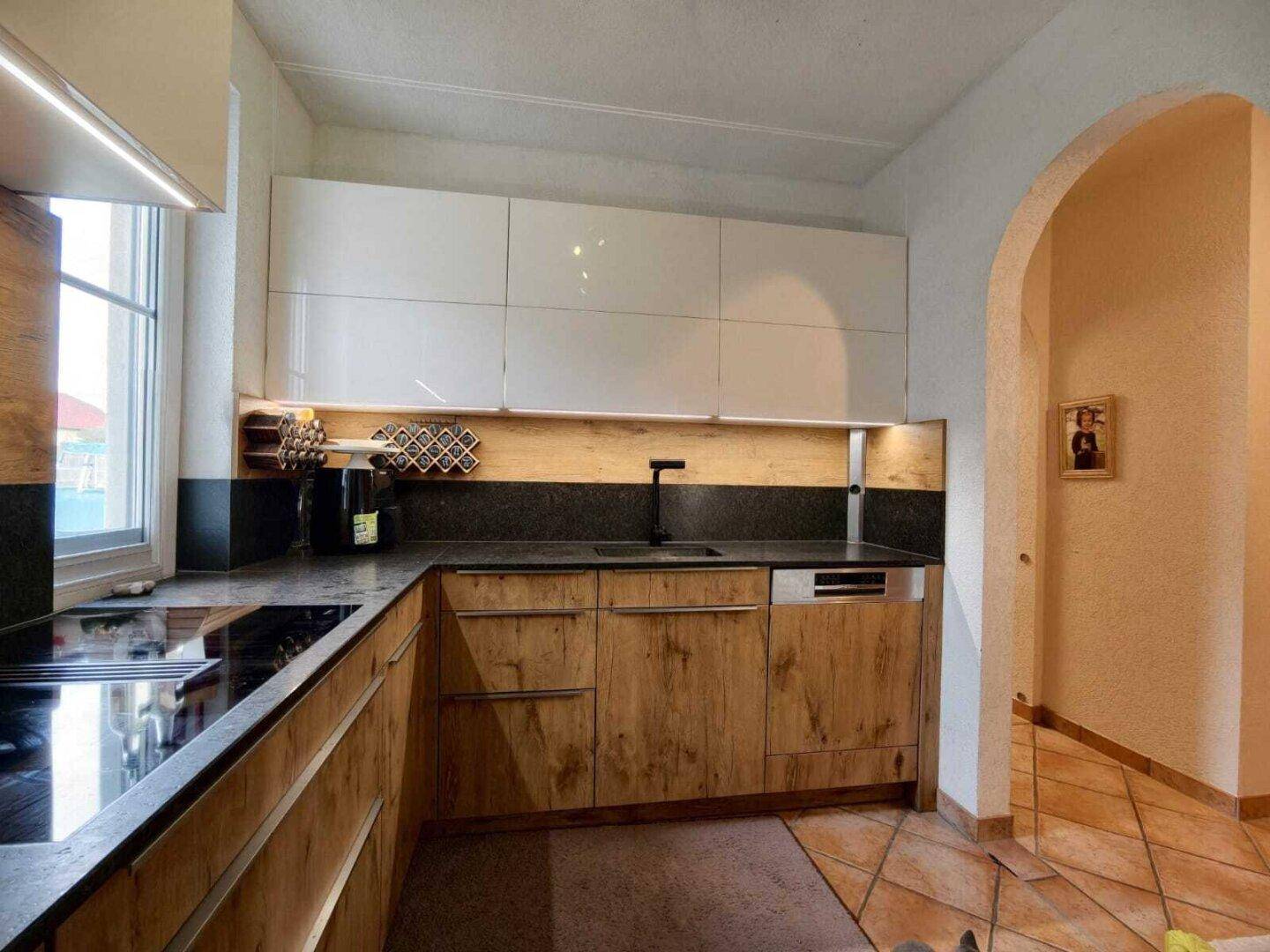 Moderne Küche mit Holzfronten, weißen Oberschränken und dunkler Arbeitsplatte.