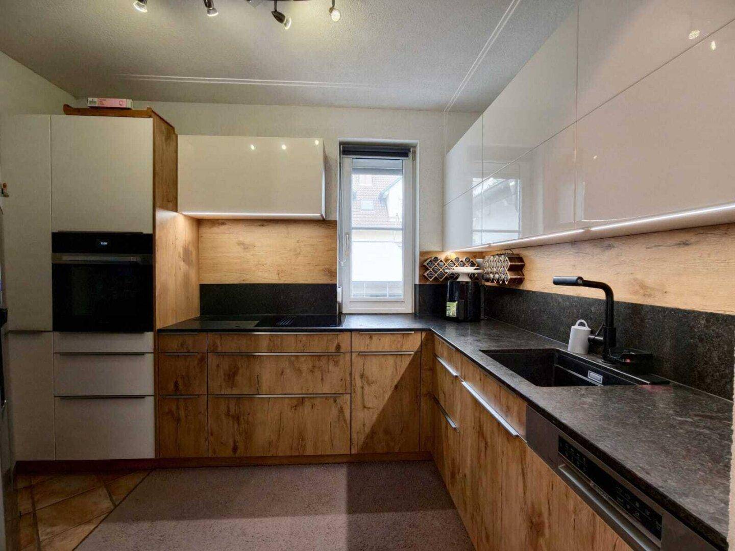 Gut ausgestattete Küche mit integrierten Geräten, Holz- und Hochglanzfronten sowie Fenster.