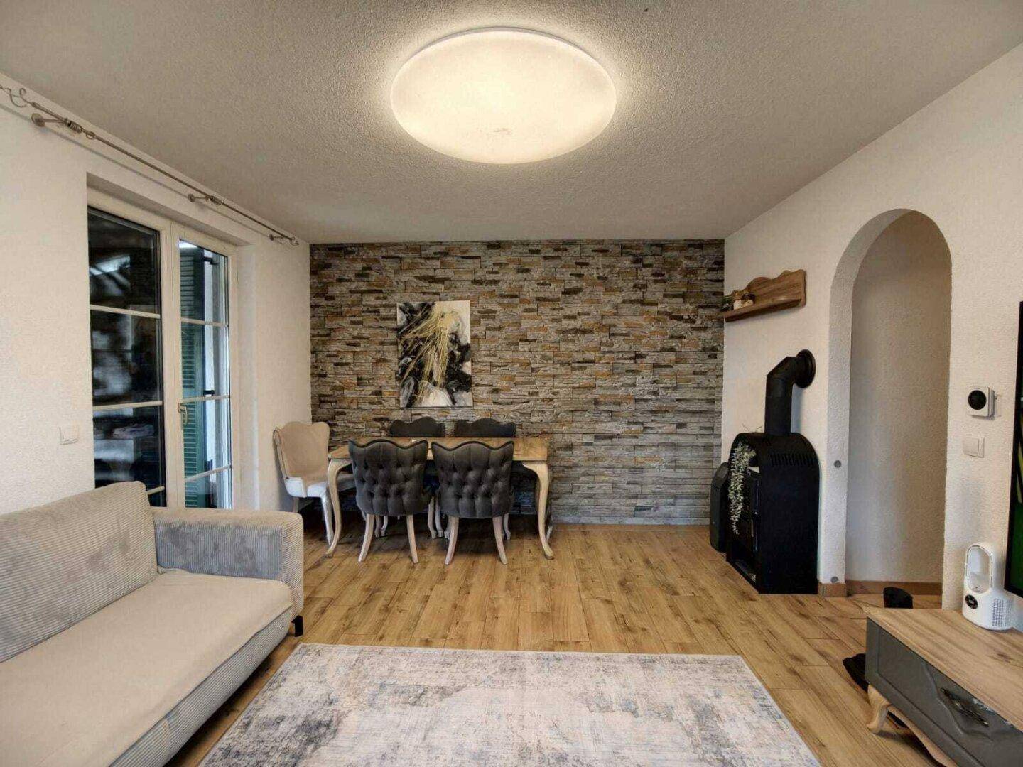 Gemütlicher Wohn- und Essbereich mit Holzboden, Steinwand und einem Holzofen.