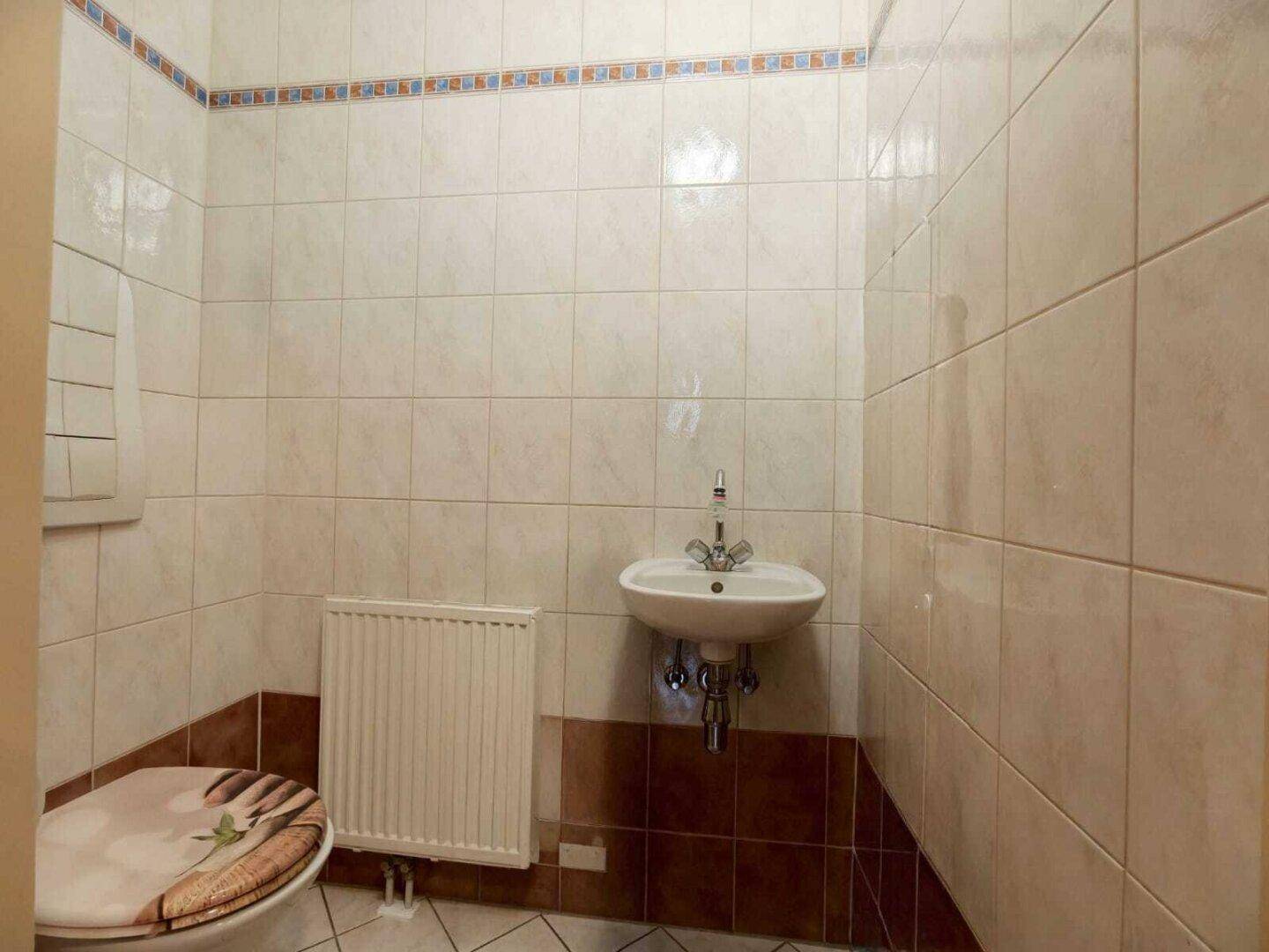 Kleines Gäste-WC mit Fliesen an Wänden und Boden sowie einem Heizkörper.