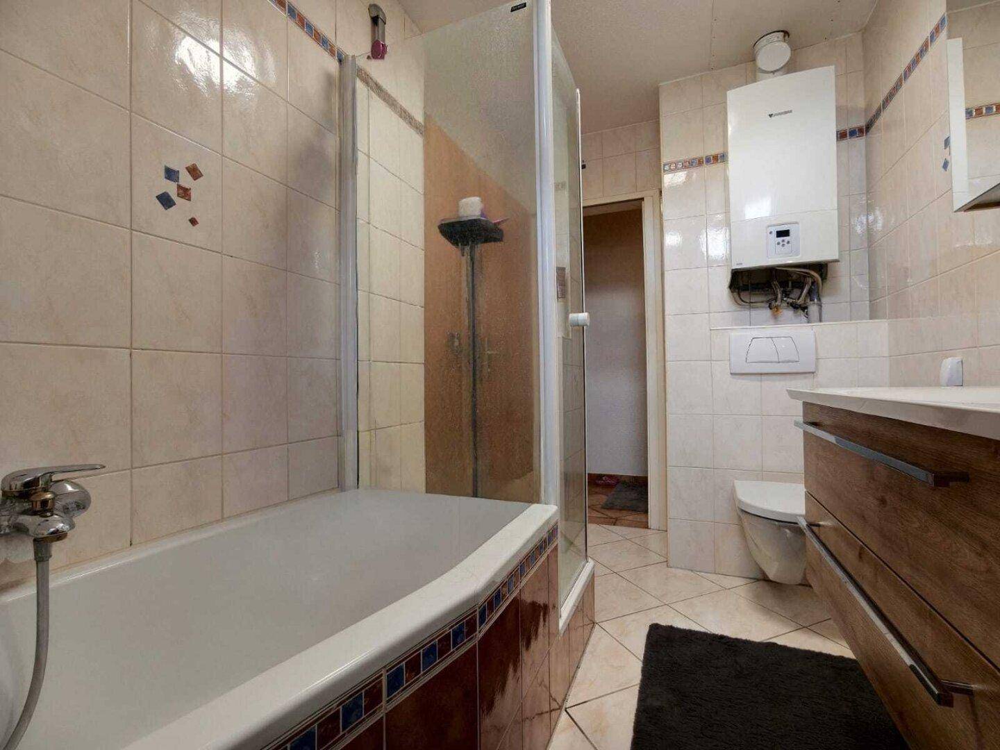 Badezimmer mit Badewanne, Dusche, Toilette und Gastherme an der Wand.