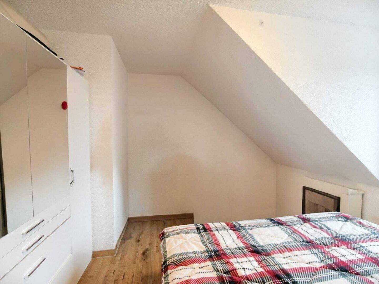 Schlafzimmer mit Holzboden, weißem Kleiderschrank und charakteristischer Dachschräge.