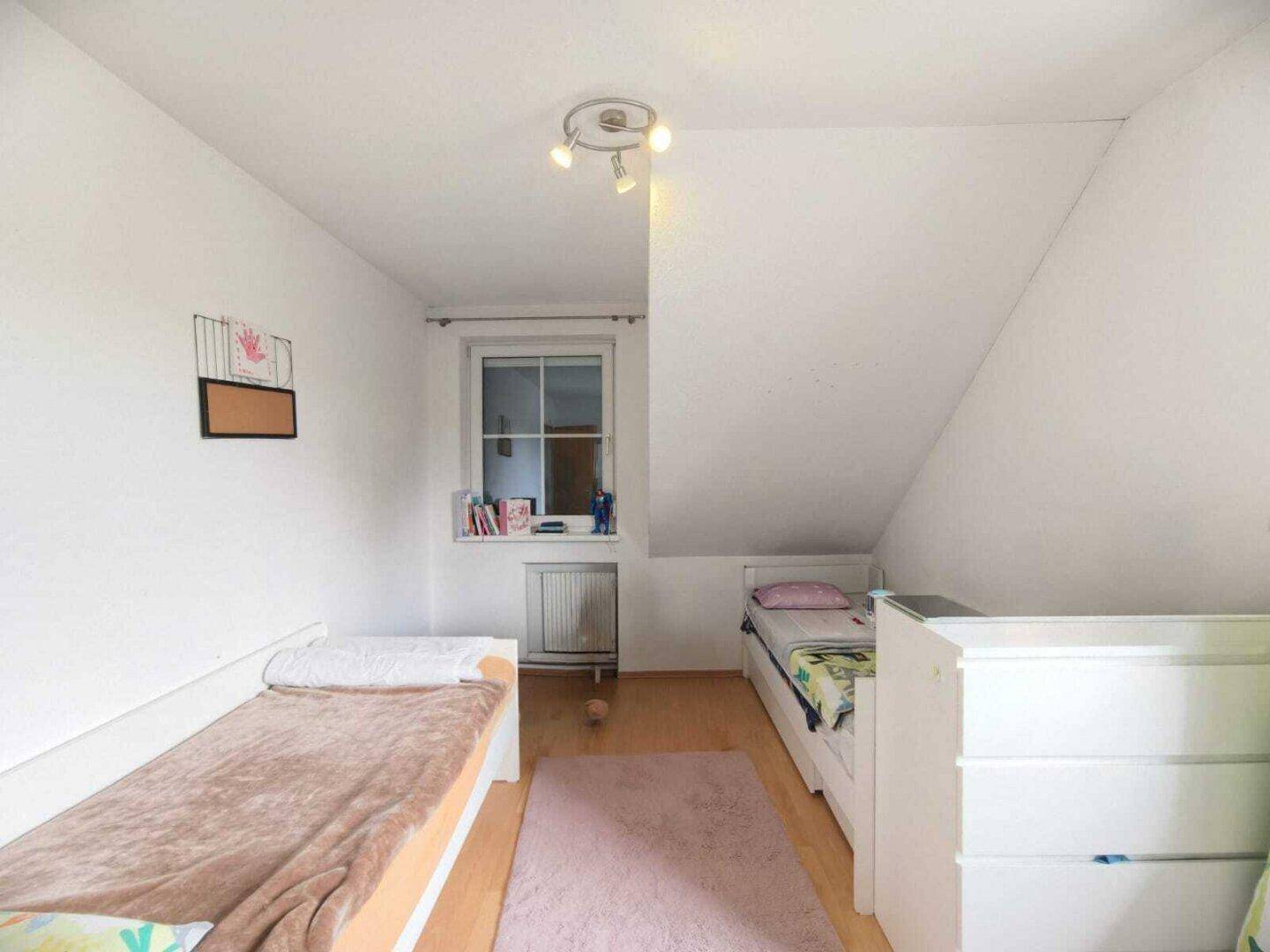 Helles Kinderzimmer mit zwei Betten, Holzboden und einem Fenster.