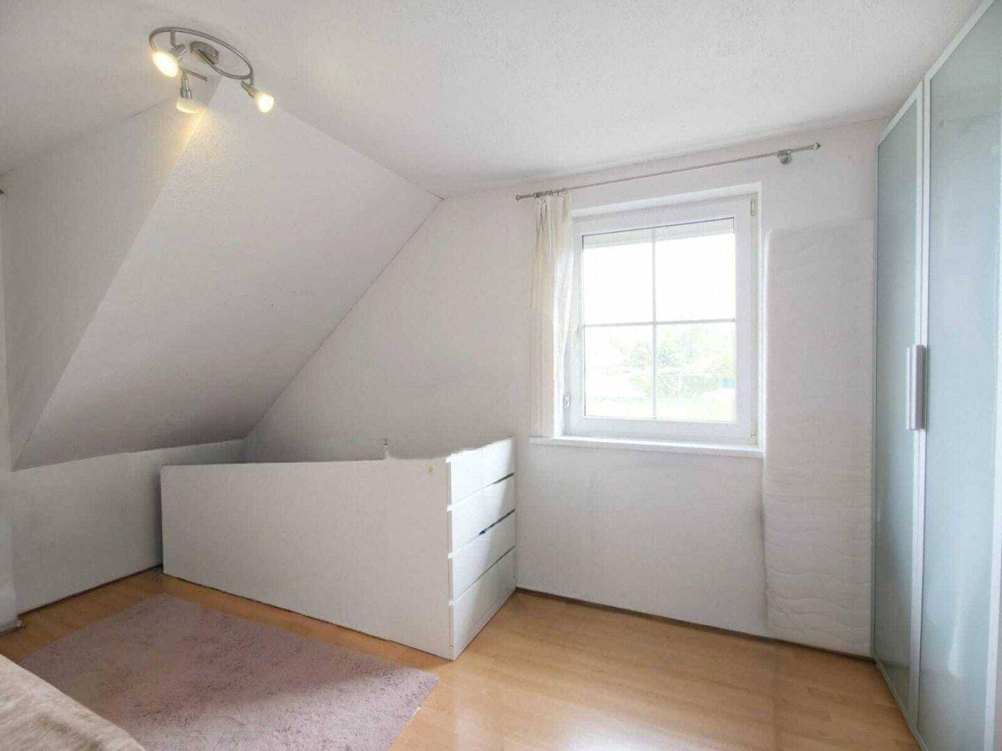Schlafzimmer mit Holzboden, Dachschräge und einem Fenster, das viel Licht hereinlässt.